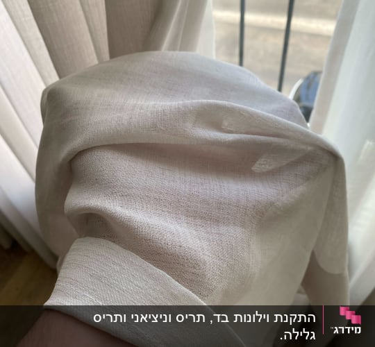 יד מחזיקה וילון לבן ליד חלון
